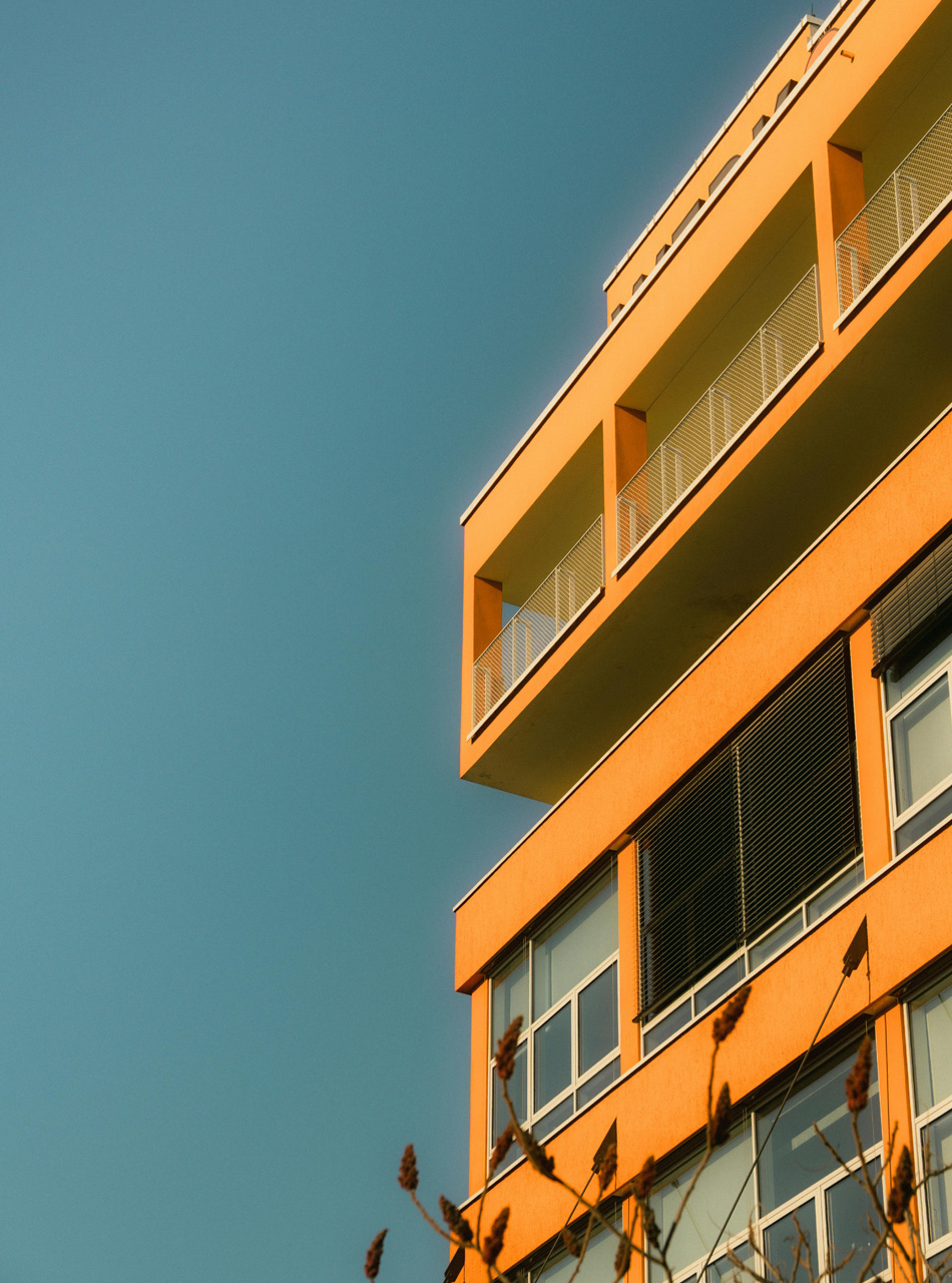 Exterior view of a contemporary multifamily apartment building with bright orange facade and open balconies.